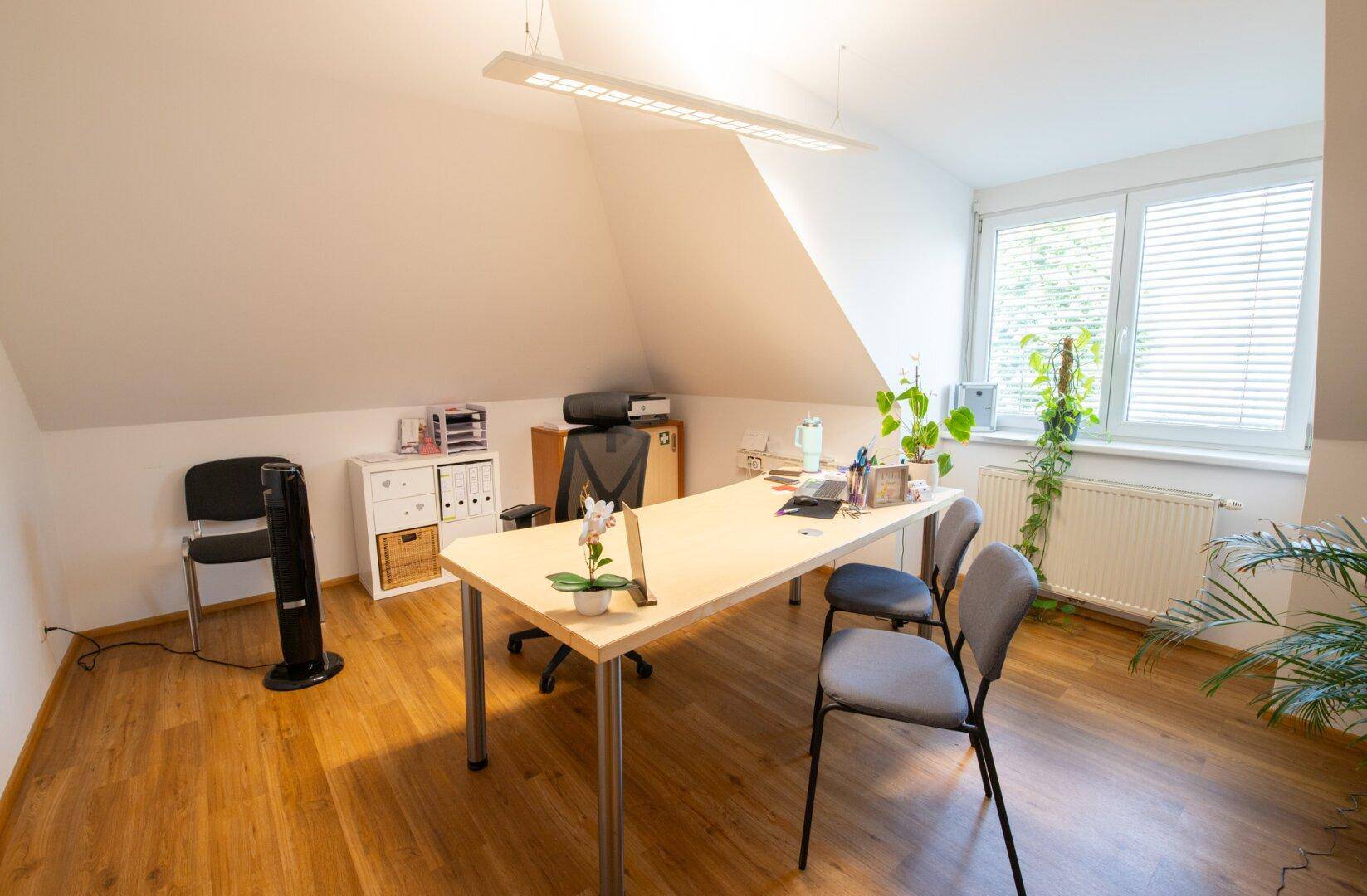 Helles Büro unter einer Dachschräge mit großem Schreibtisch, Bürostuhl und Pflanzen, ideal für konzentriertes Arbeiten.