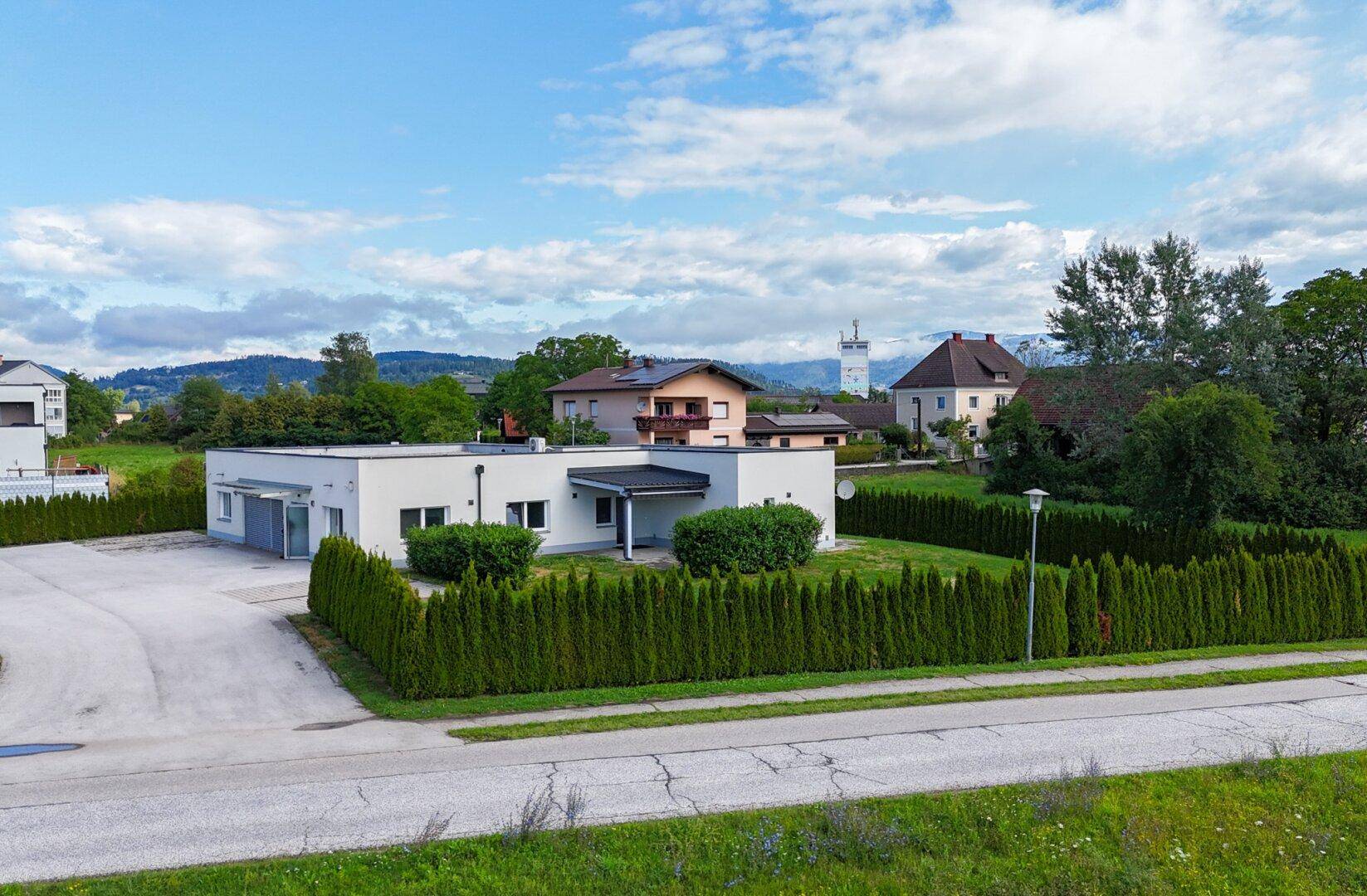 Weitläufige Ansicht eines modernen Gebäudes mit umliegender Grünfläche und Hecken, im Hintergrund Berge.