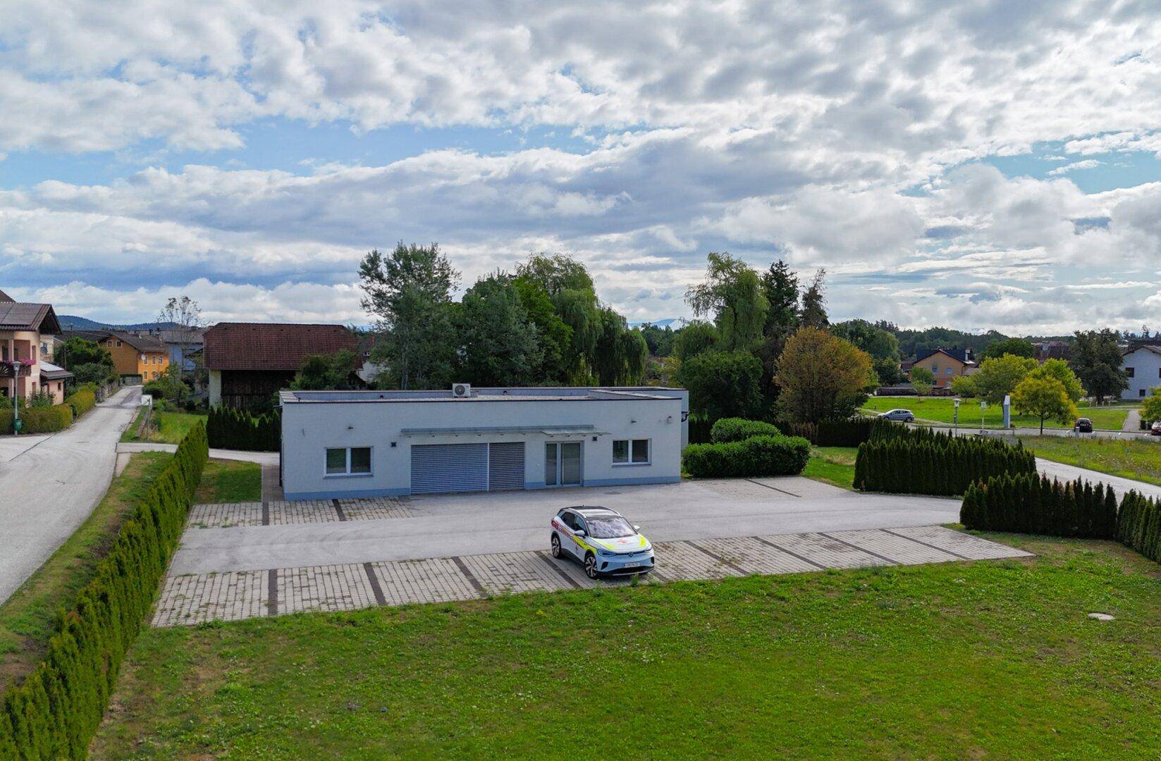 Vogelperspektive eines modernen Gebäudes mit Parkplätzen und einer Hecke, eingebettet in eine grüne Umgebung.