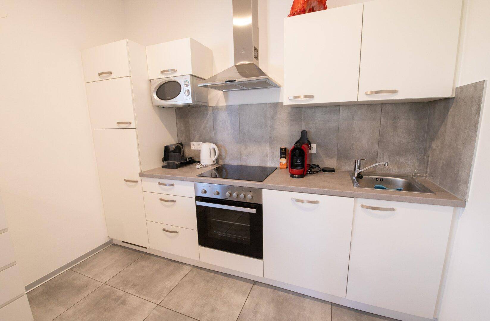 Kompakte, moderne Küche mit weißen Schränken, Induktionskochfeld und Edelstahl-Dunstabzugshaube.