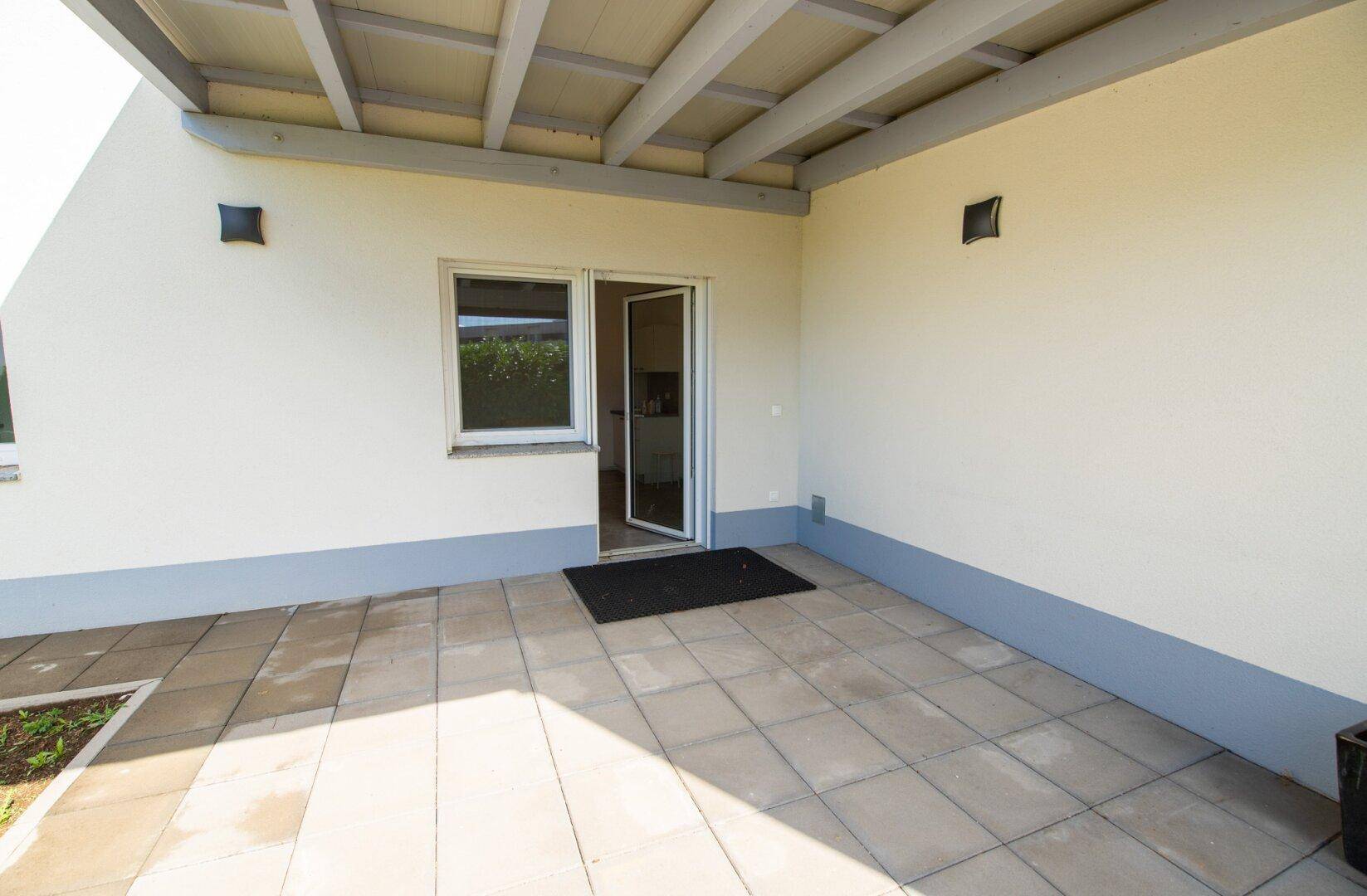 Überdachte Terrasse mit Zugang zum Innenbereich und Blick auf den Garten.