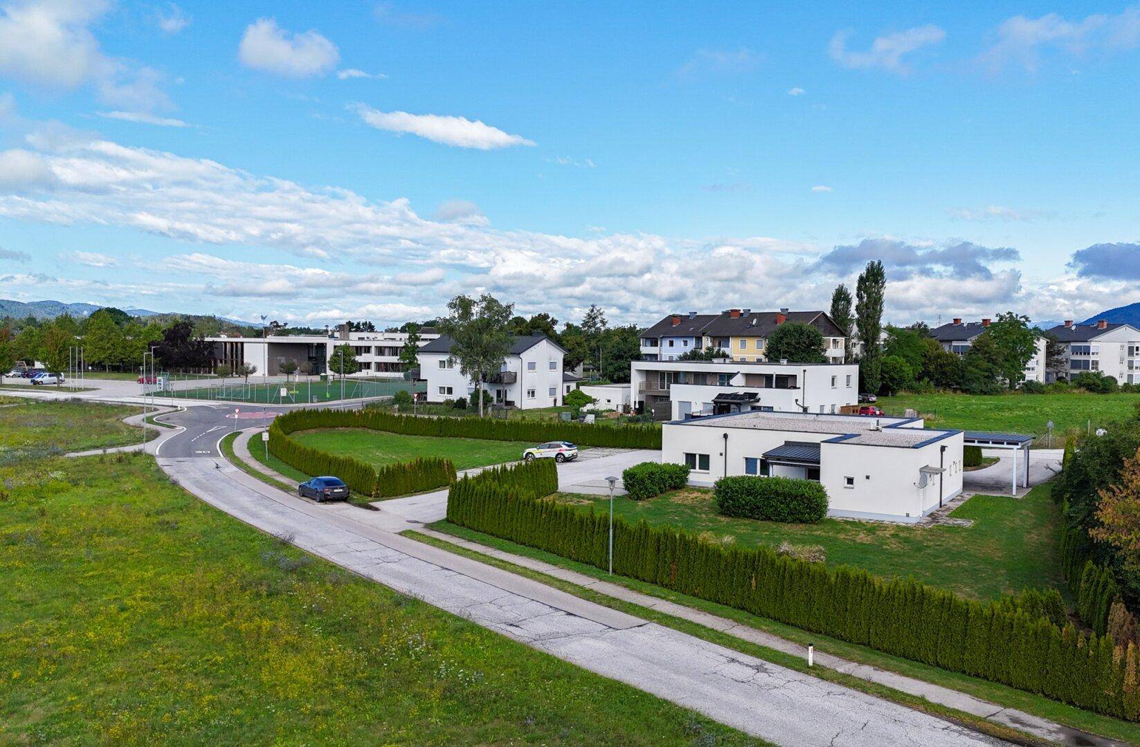 Weitläufige Luftaufnahme eines modernen Gebäudekomplexes mit viel Grün und umliegender Infrastruktur.