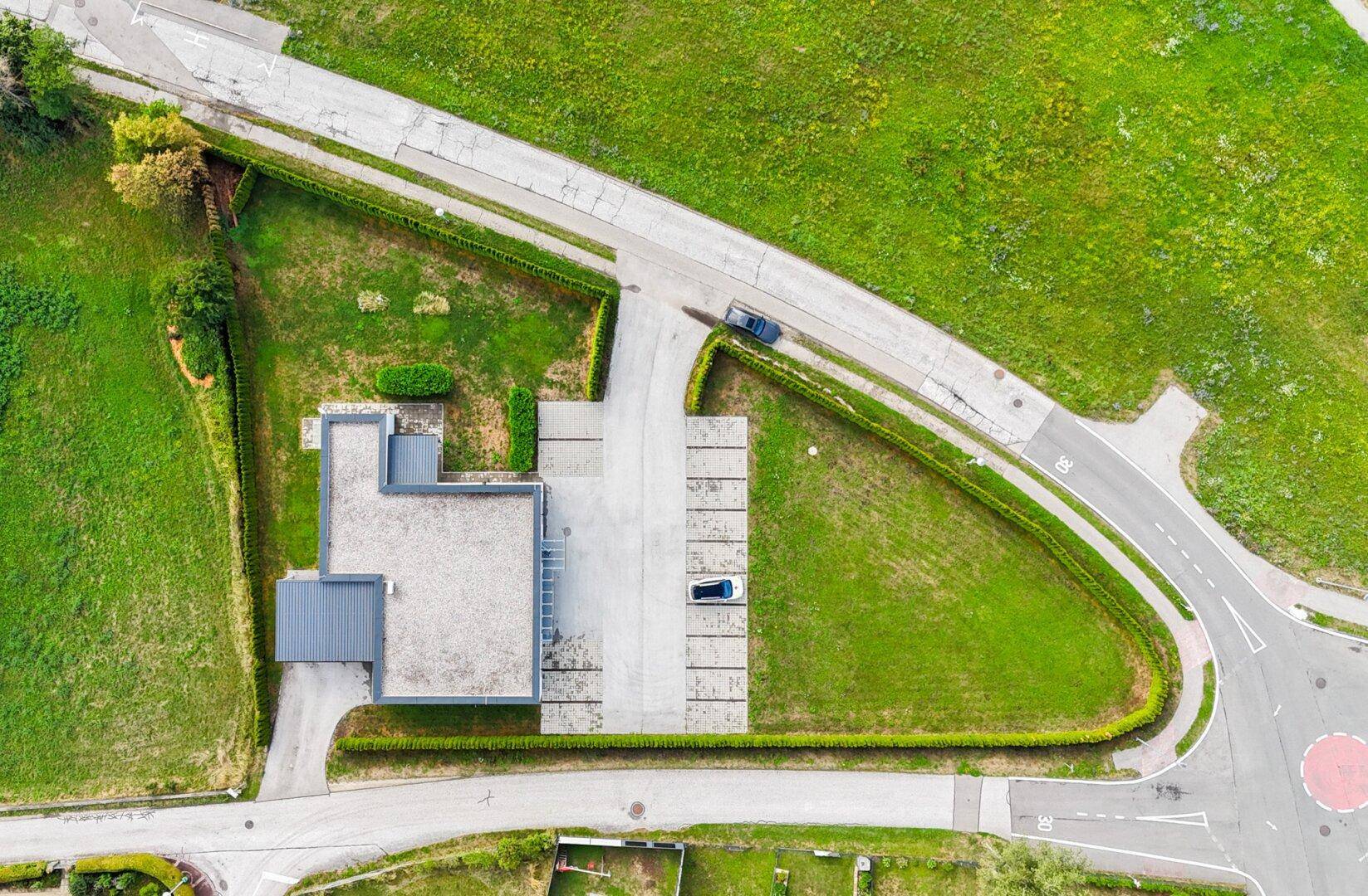 Luftaufnahme eines modernen Gebäudes mit Flachdach, umgeben von Grünflächen und einem Parkplatz.