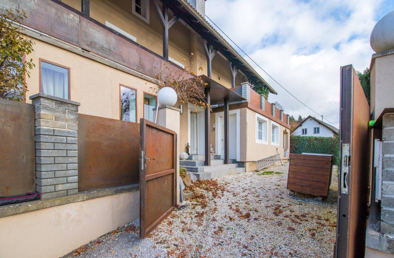 Eingangsbereich des Hauses mit rustikalen Metalltoren und Kiesweg, umgeben von Herbstlaub.