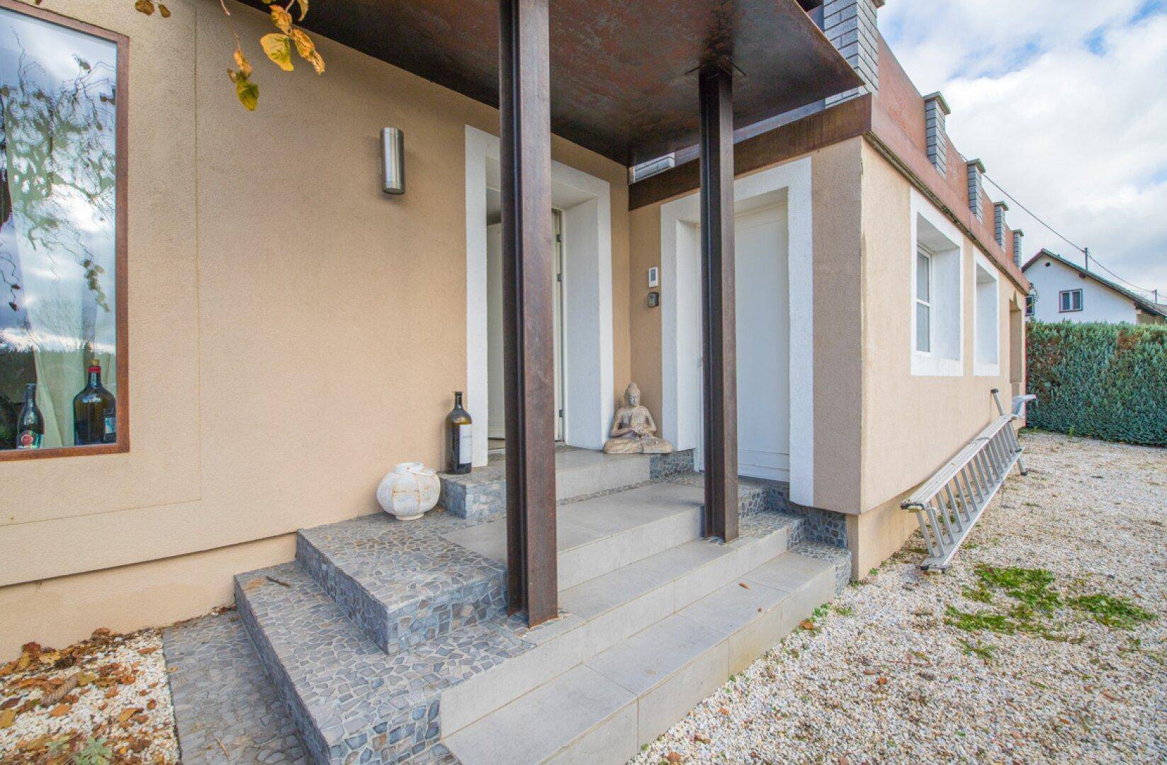 Überdachter Eingangsbereich mit Steinstufen und einer Buddha-Statue als Dekoration.