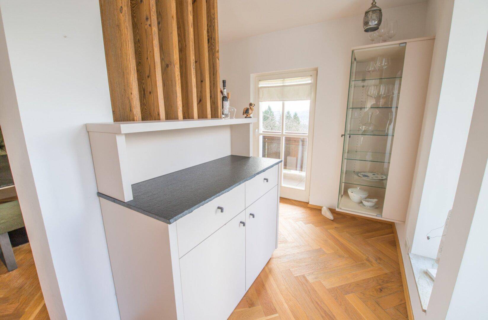 Essbereich mit Sideboard und Vitrine, daneben ein Fenster mit Blick auf die Landschaft.