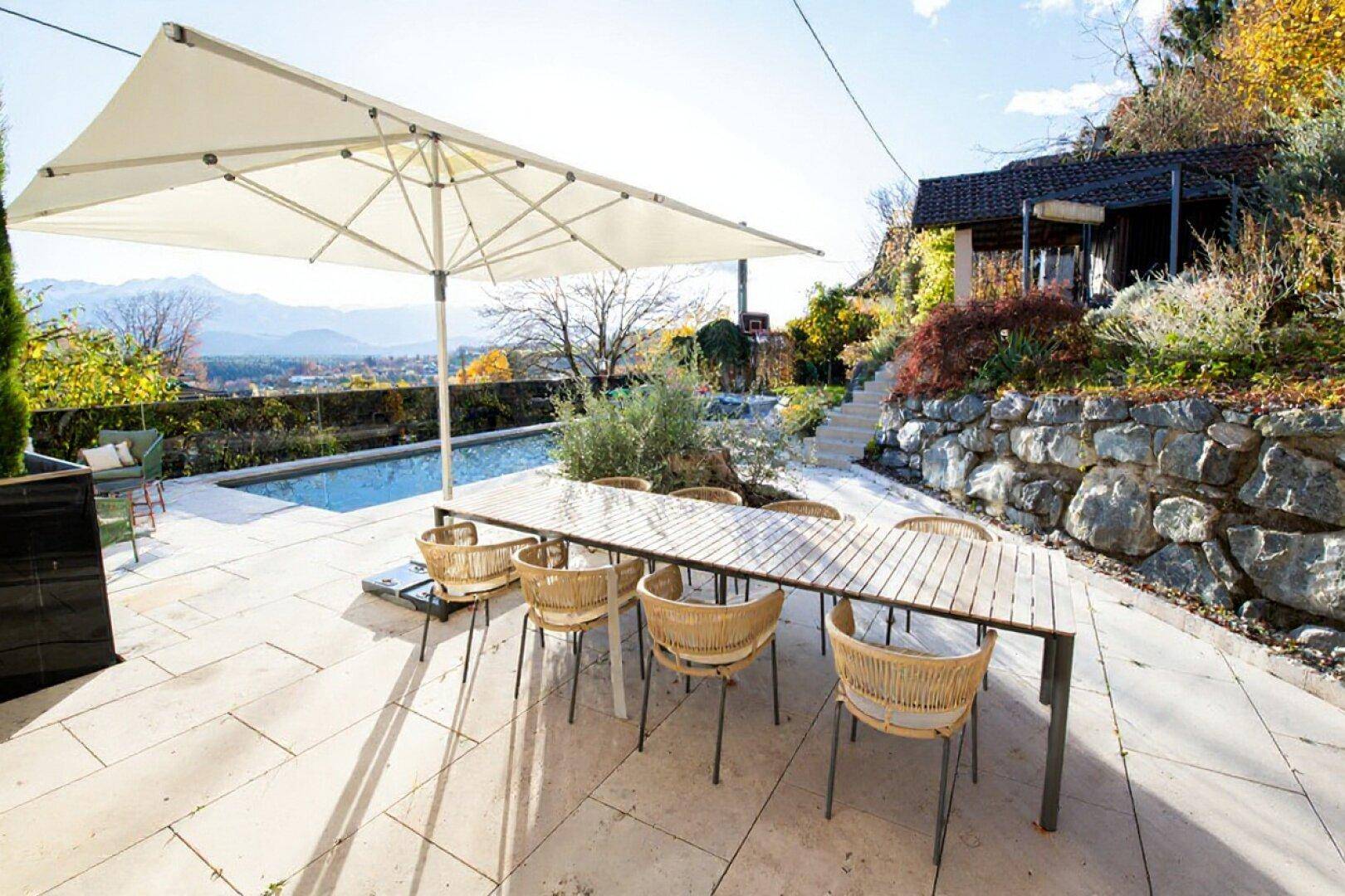Große Sonnenterrasse mit Esstisch, Stühlen und Blick auf die Berge und den Pool.