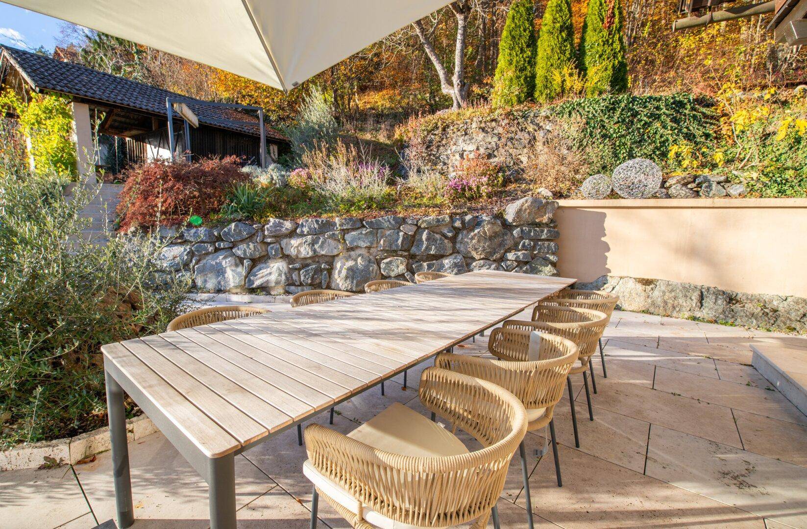 Geräumige Terrasse mit Holztisch und Korbstühlen, umgeben von mediterraner Bepflanzung.