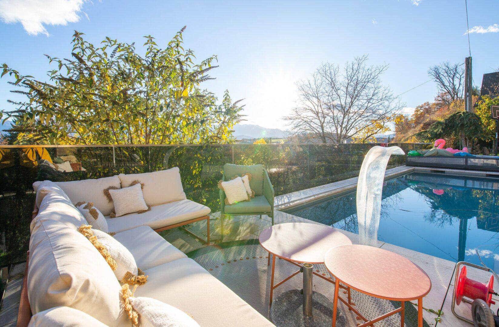 Sonnige Terrasse mit Lounge-Sofa, Beistelltischen und Blick auf den Pool und die Berge.