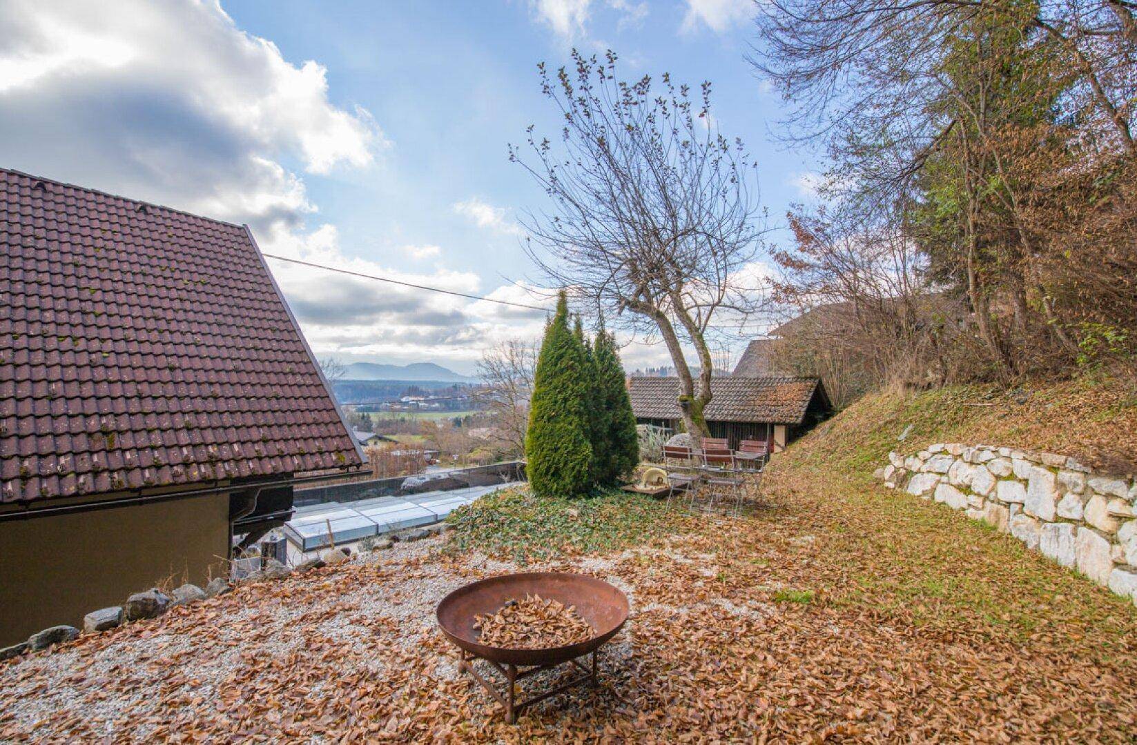 Herbstlicher Garten mit Feuerstelle, Bäumen und Blick auf die umliegende Natur.