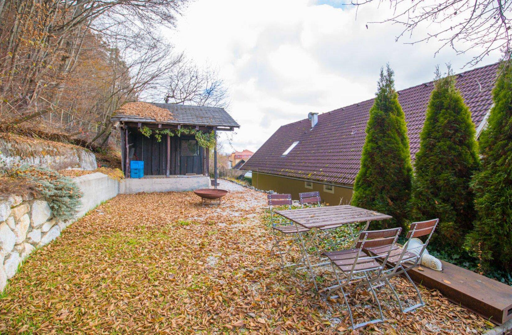 Gartenbereich mit Sitzgelegenheiten, Feuerstelle und einem kleinen Gartenhaus im Hintergrund.