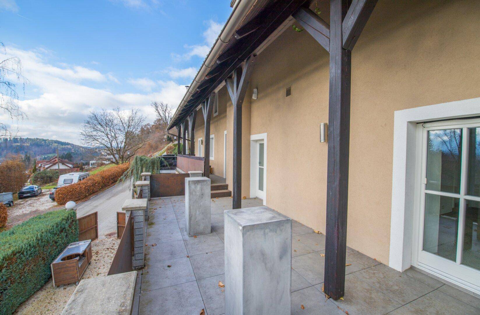 Überdachte Terrasse entlang der Hausfassade mit Blick auf die Umgebung.