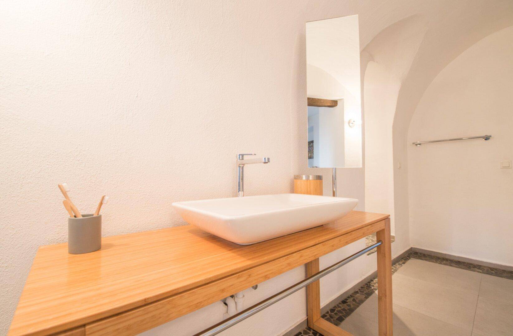 Nahaufnahme des modernen Waschbeckens auf einem Holztisch mit einem hohen Spiegel im Badezimmer.