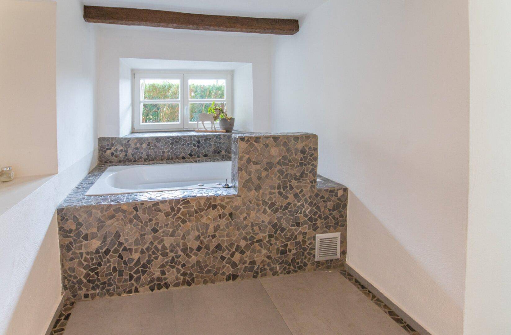 Eingebauter Whirlpool mit Mosaikfliesen und einem Fenster, das natürliches Licht hereinlässt.