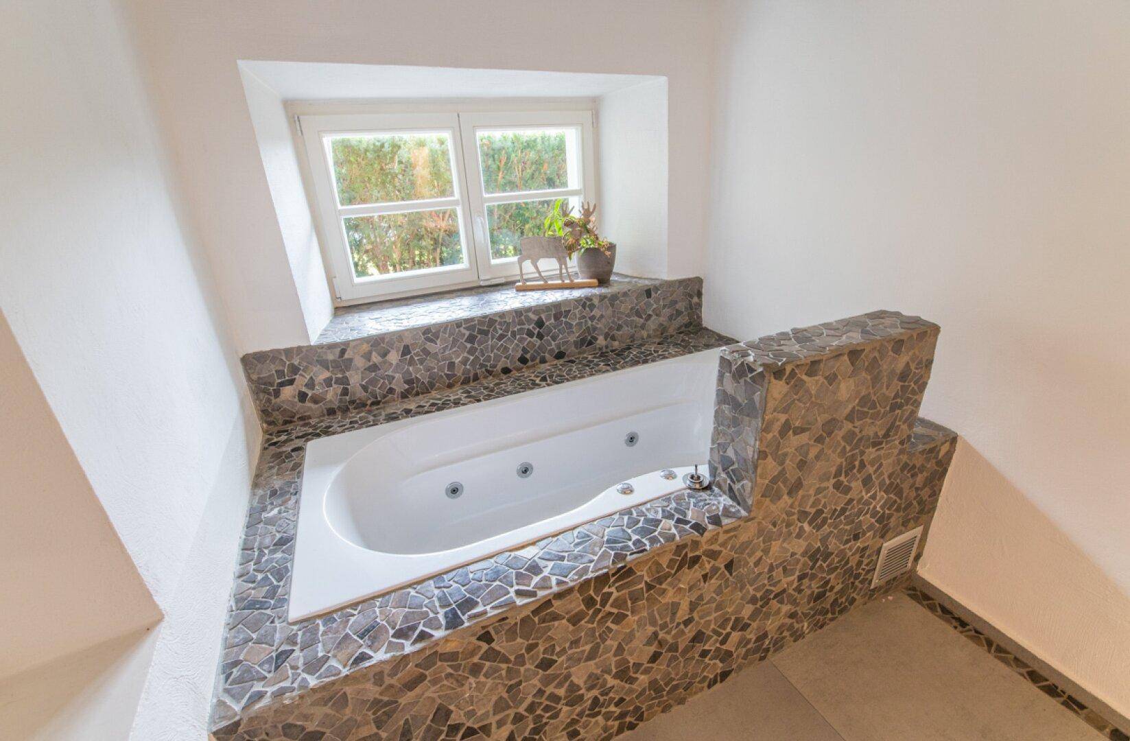 Detailansicht des eingebauten Whirlpools mit Mosaikfliesen und einem Fenster für natürliche Belichtung.