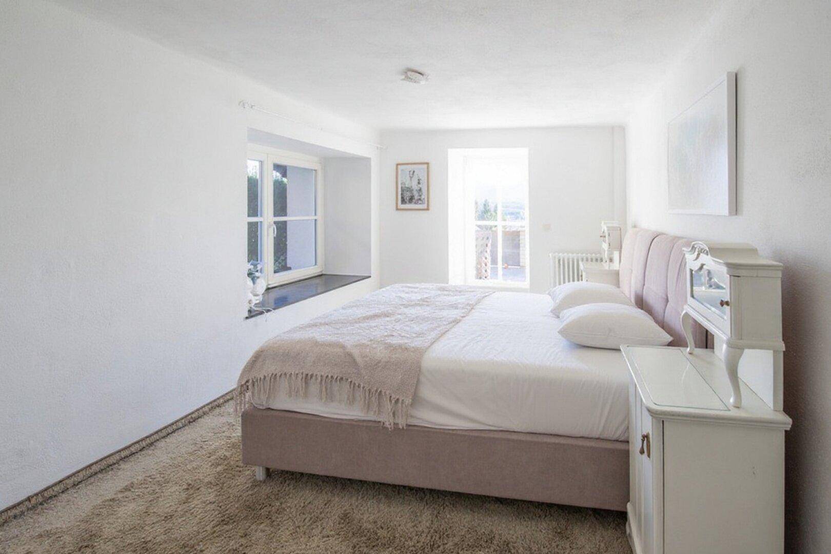 Helles Schlafzimmer mit einem bequemen Bett, weißen Wänden und einem großen Fenster.