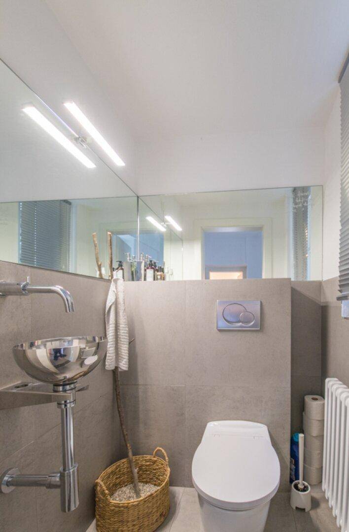 Modernes WC mit wandmontierter Toilette, einzigartigem Waschbecken und großem Spiegel.