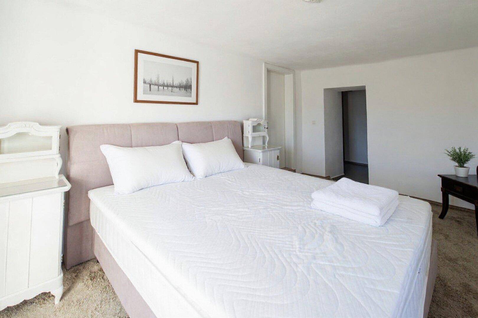 Gemütliches Schlafzimmer mit einem großen Bett, weißen Wänden und weichem Teppichboden.
