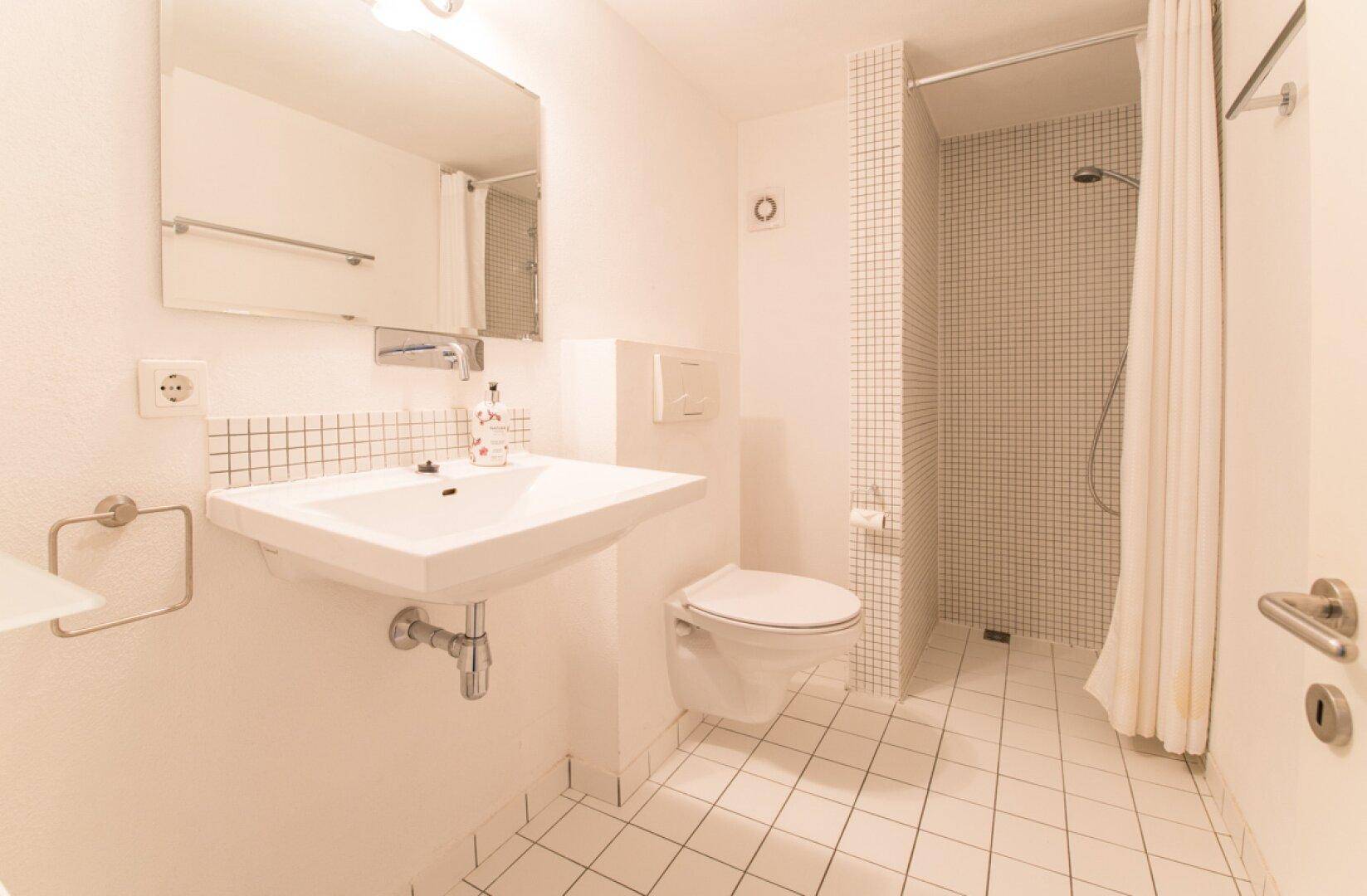 Modernes Badezimmer mit weißen Fliesen, Waschbecken, Toilette und Duschbereich.