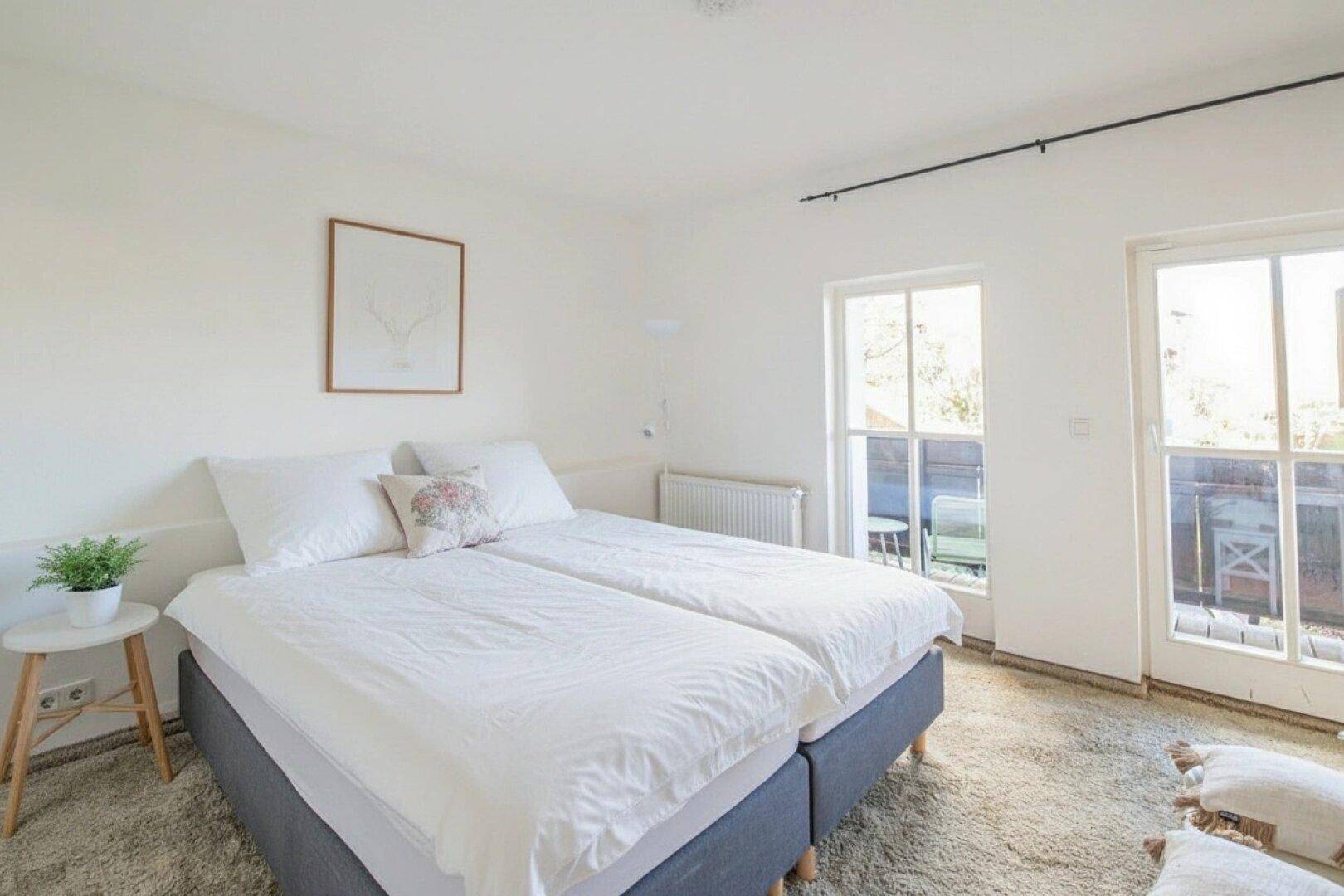 Helles Schlafzimmer mit zwei Einzelbetten, Fenster und Zugang zu einem Außenbereich.