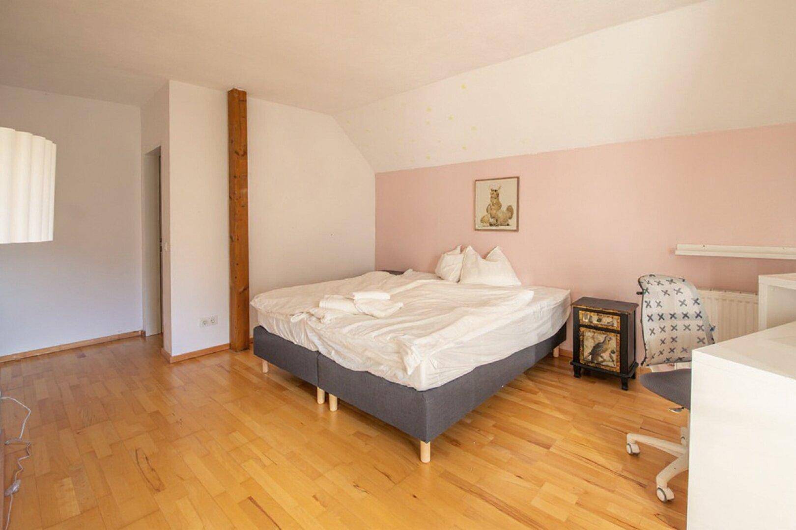 Schlafzimmer mit Holzboden, rosa Akzentwand und schräger Decke.