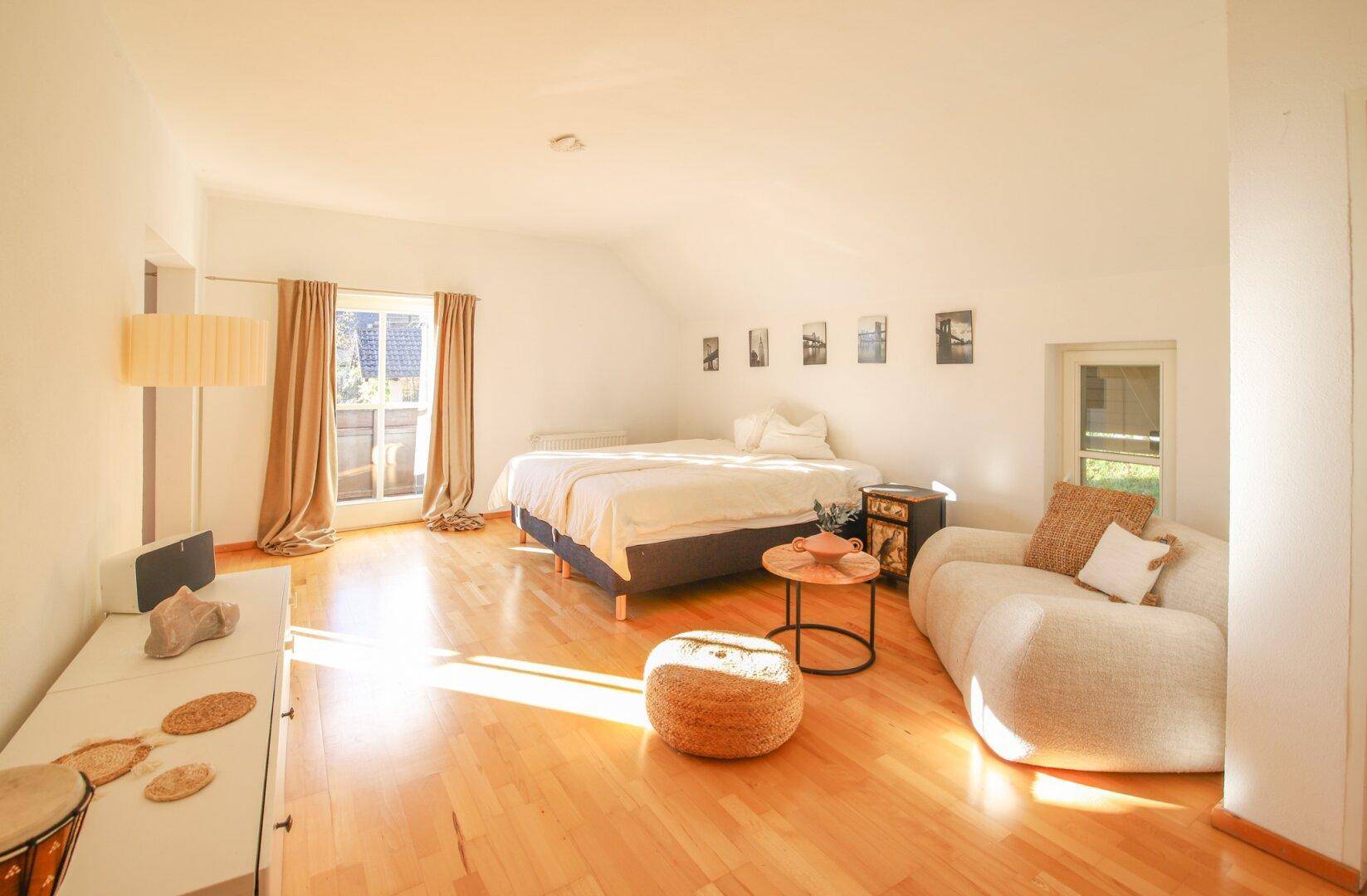 Lichtdurchflutetes Schlafzimmer mit Holzboden, Sofa und schräger Decke.