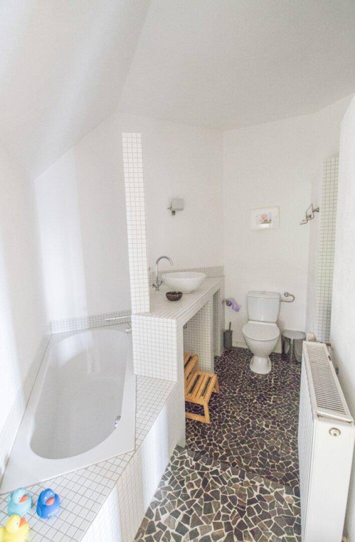 Badezimmer mit Badewanne, Waschbecken, Toilette und Mosaikboden unter schräger Decke.