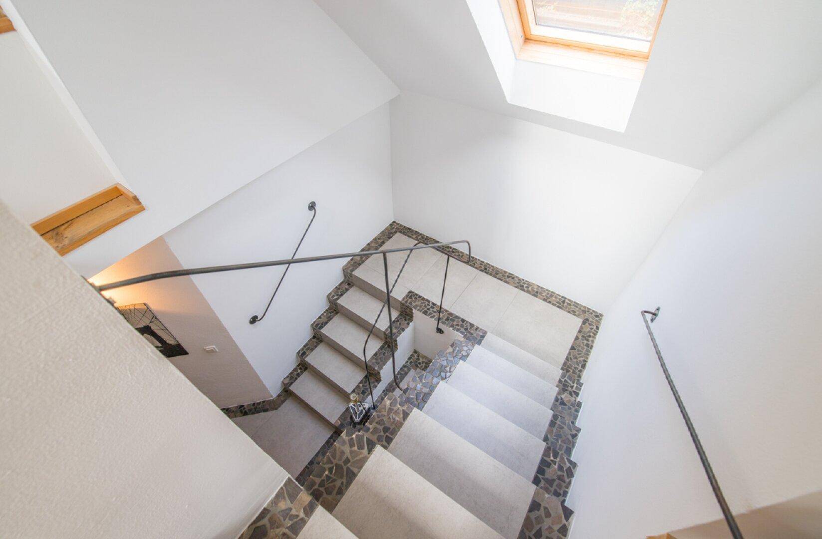Blick von oben auf eine Treppe mit einem hellen Oberlicht, das den Bereich erhellt.