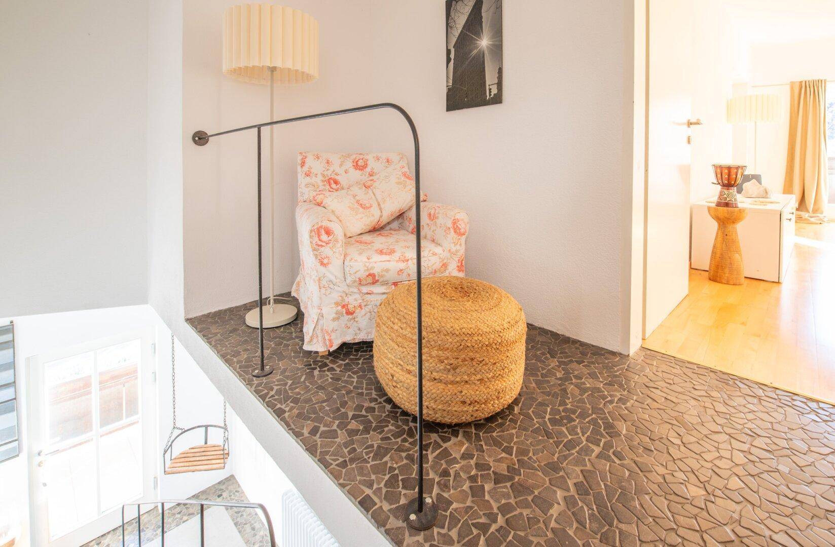 Gemütlicher Treppenabsatz mit Sessel, Hocker und Blick in einen angrenzenden Wohnbereich.