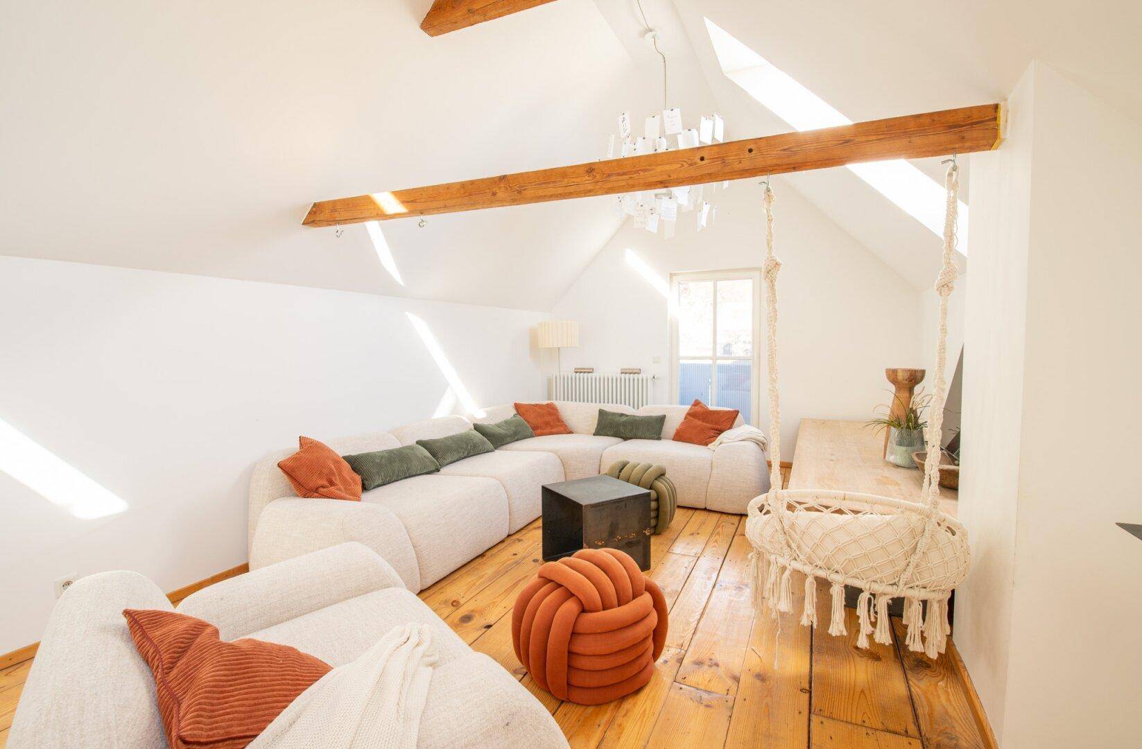 Gemütliches Wohnzimmer im Dachgeschoss mit Holzbalken, großem Sofa und Schaukelstuhl.
