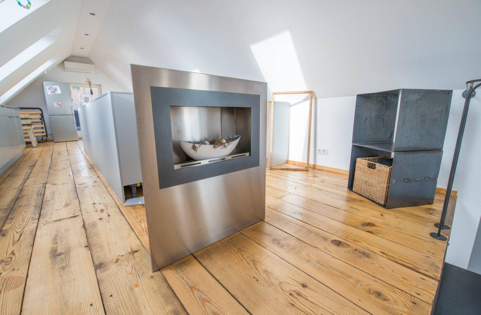 Heller Dachbodenbereich mit Holzdielenboden und einem modernen Kamin als Blickfang.