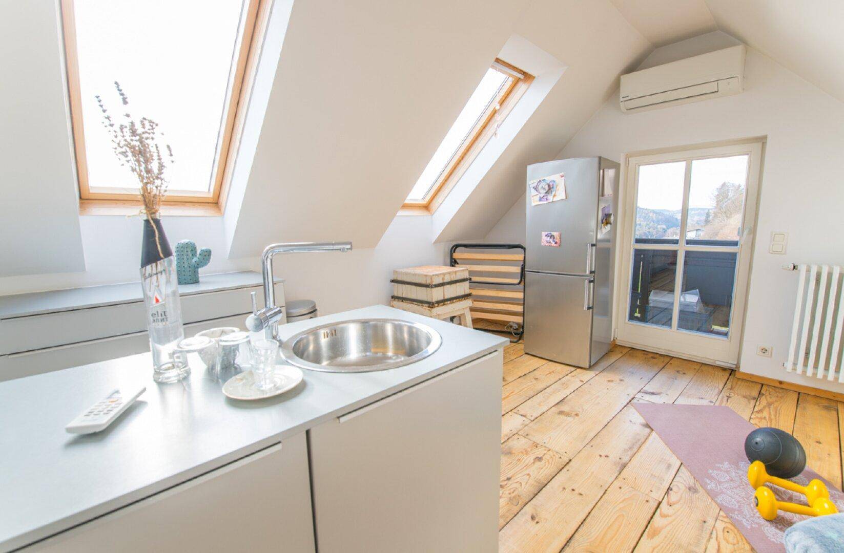 Helle Dachgeschosswohnung mit kleiner Küchenzeile, Dachfenstern und Zugang zu einem Balkon.