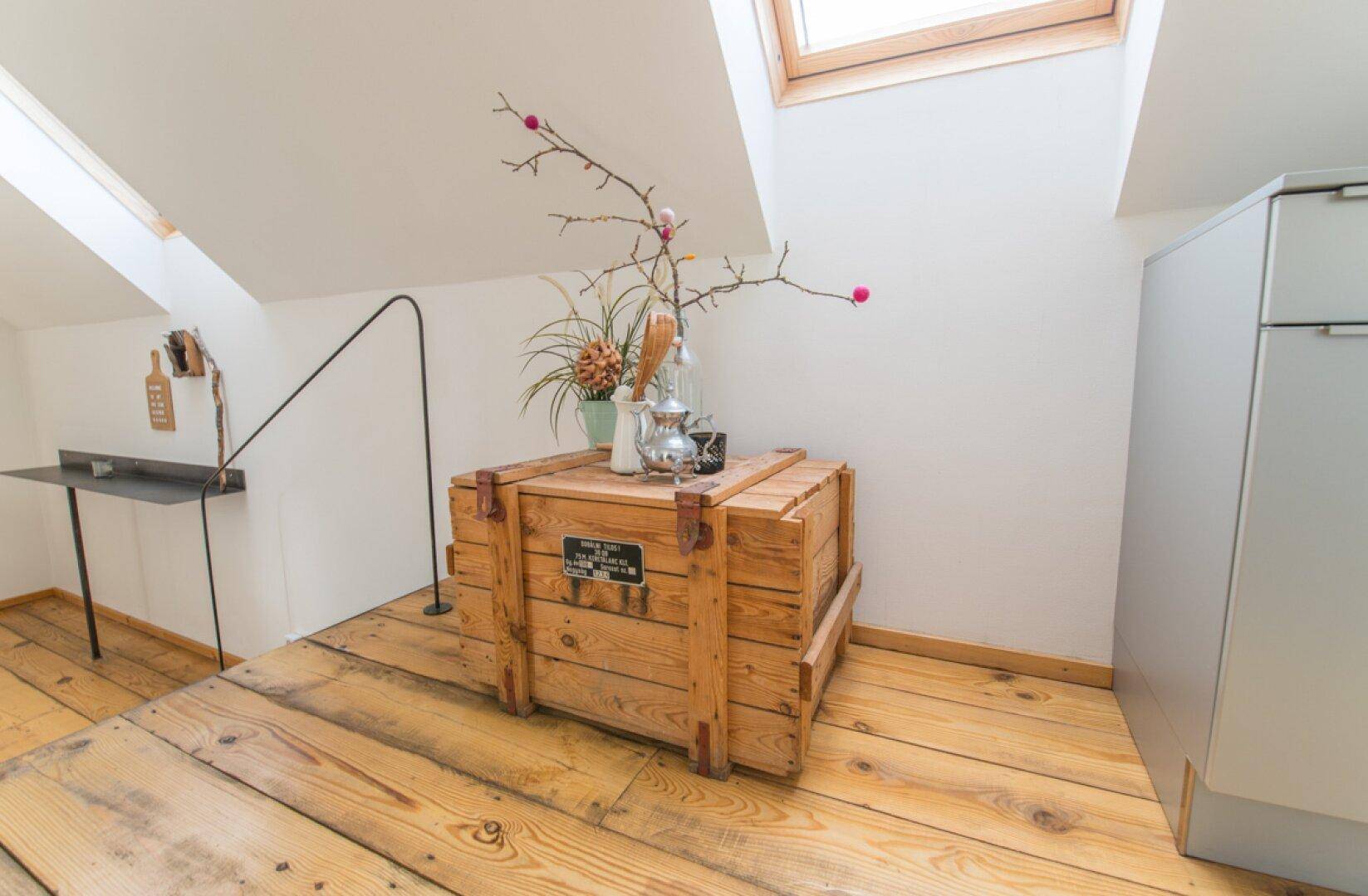 Heller Dachgeschossbereich mit Holzboden, Dachfenster und einer dekorativen Holzkiste als Ablage.