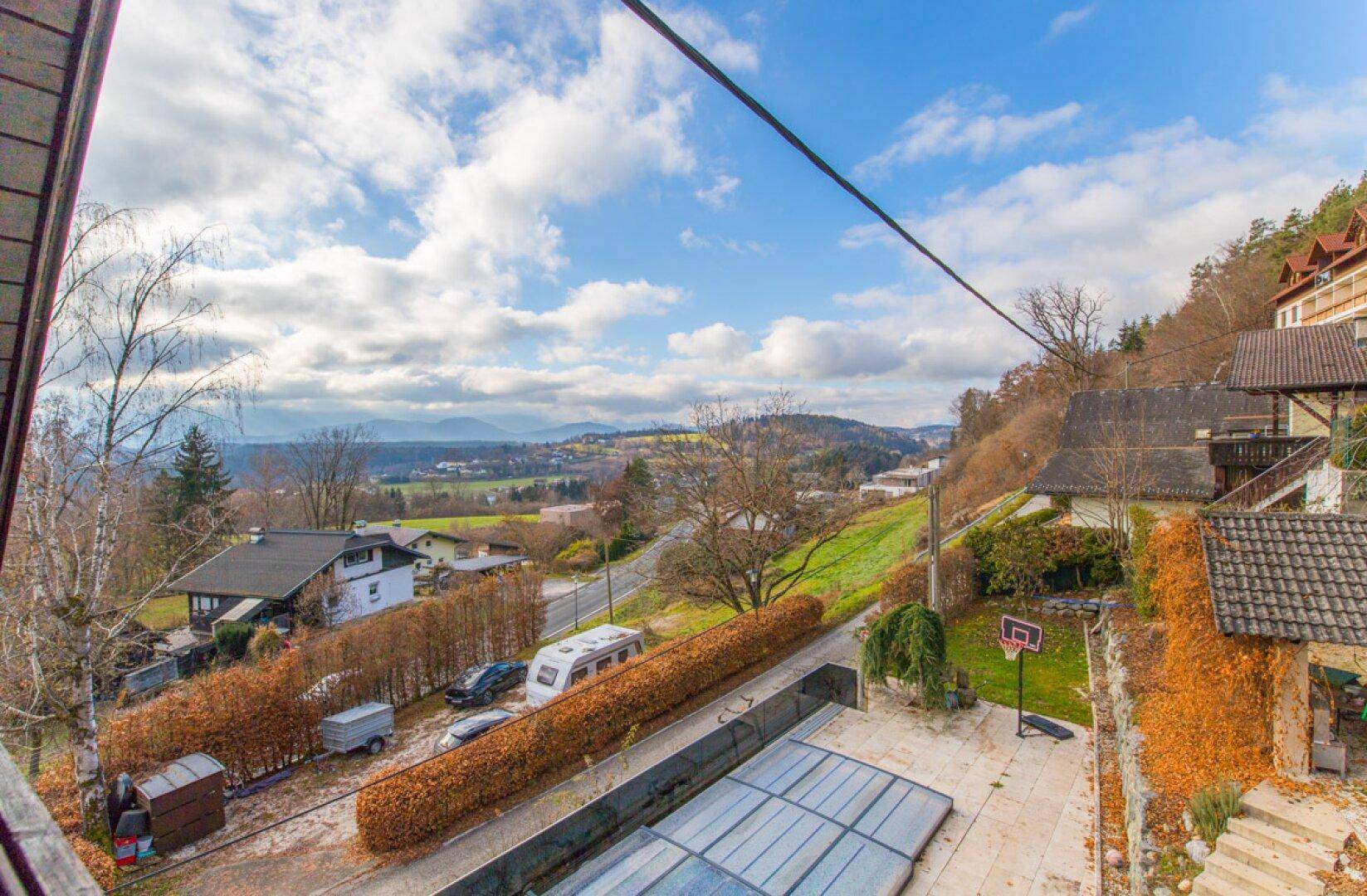 Weitläufiger Blick über die hügelige Landschaft mit Häusern, Bergen und einem Wohnwagen auf der Straße.