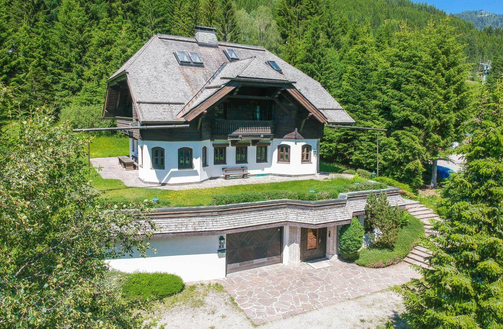Traditionelles Chalet-Haus in alpiner Umgebung, umgeben von dichtem Wald und mit integrierter Garage.