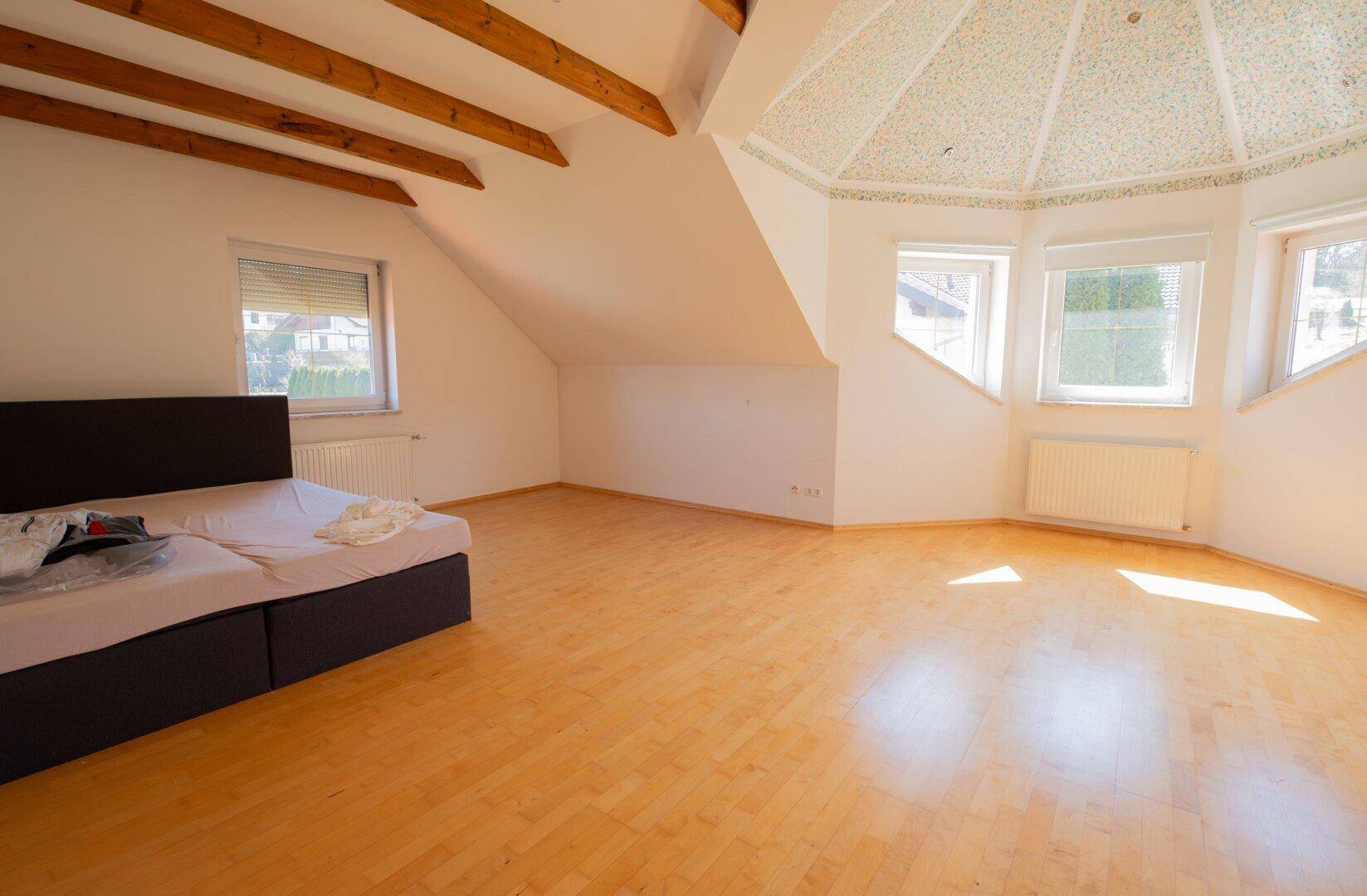 Geräumiges Schlafzimmer mit Parkettboden, sichtbaren Holzbalken und einer dekorativen Kuppeldecke.