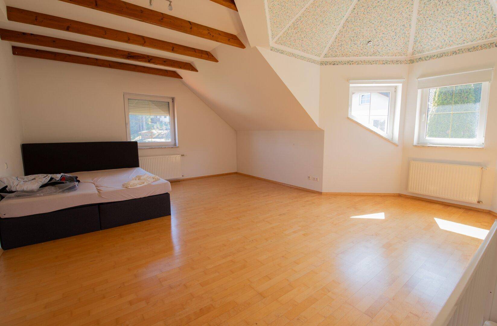 Helles Schlafzimmer im Dachgeschoss mit Parkettboden, Holzbalken und einer besonderen Kuppeldecke.