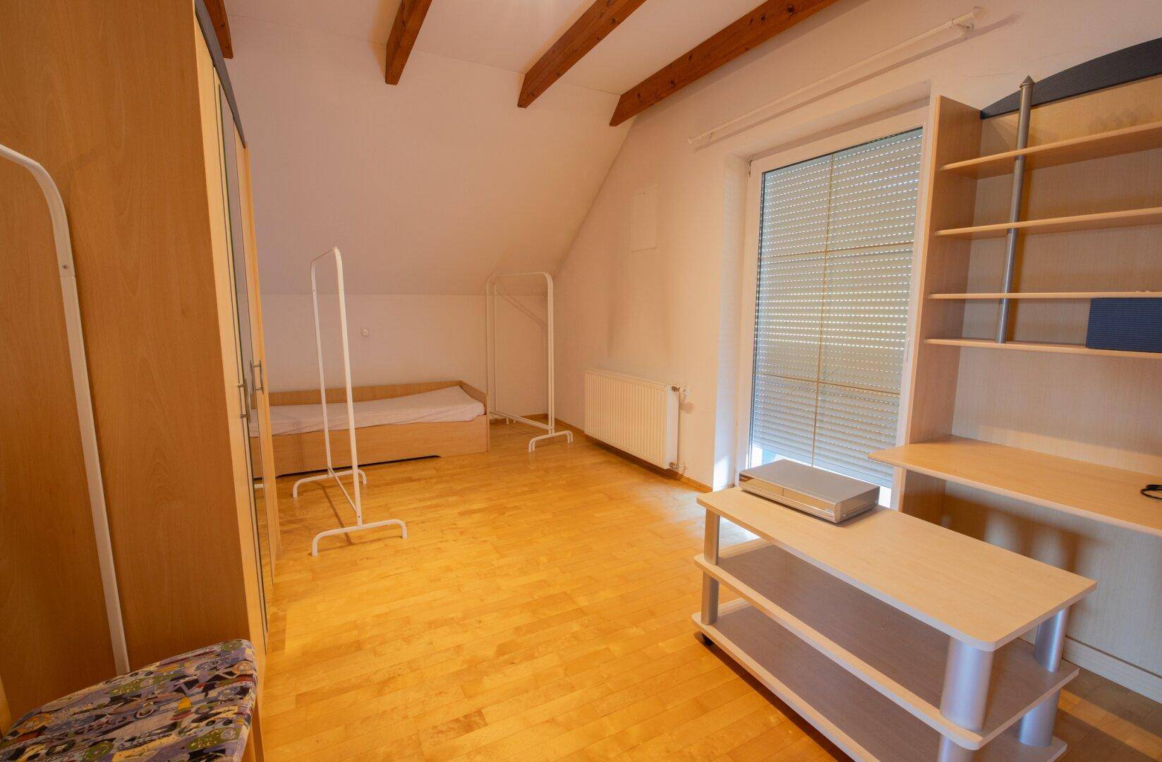 Zimmer im Dachgeschoss mit Parkettboden, Schrank und Zugang zu einem Balkon.