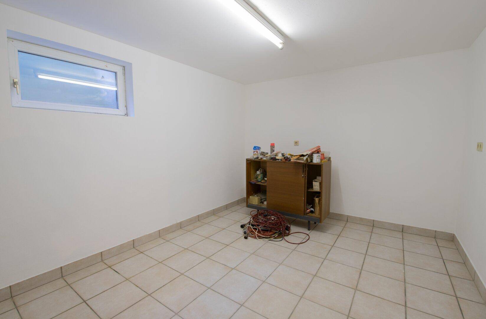 Praktischer Kellerraum mit Fliesenboden und Fenster, geeignet als Abstell- oder Werkraum.