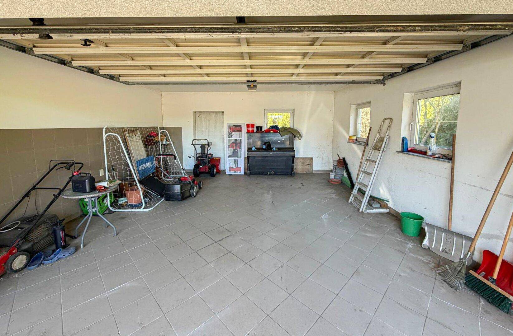 Geräumige Garage mit Fliesenboden und Fenstern, bietet Platz für Fahrzeuge und Gartengeräte.