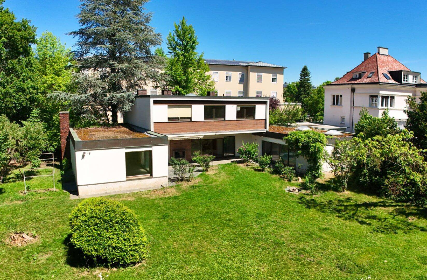 Modernes Haus mit Flachdach und großem Gartenbereich unter blauem Himmel.