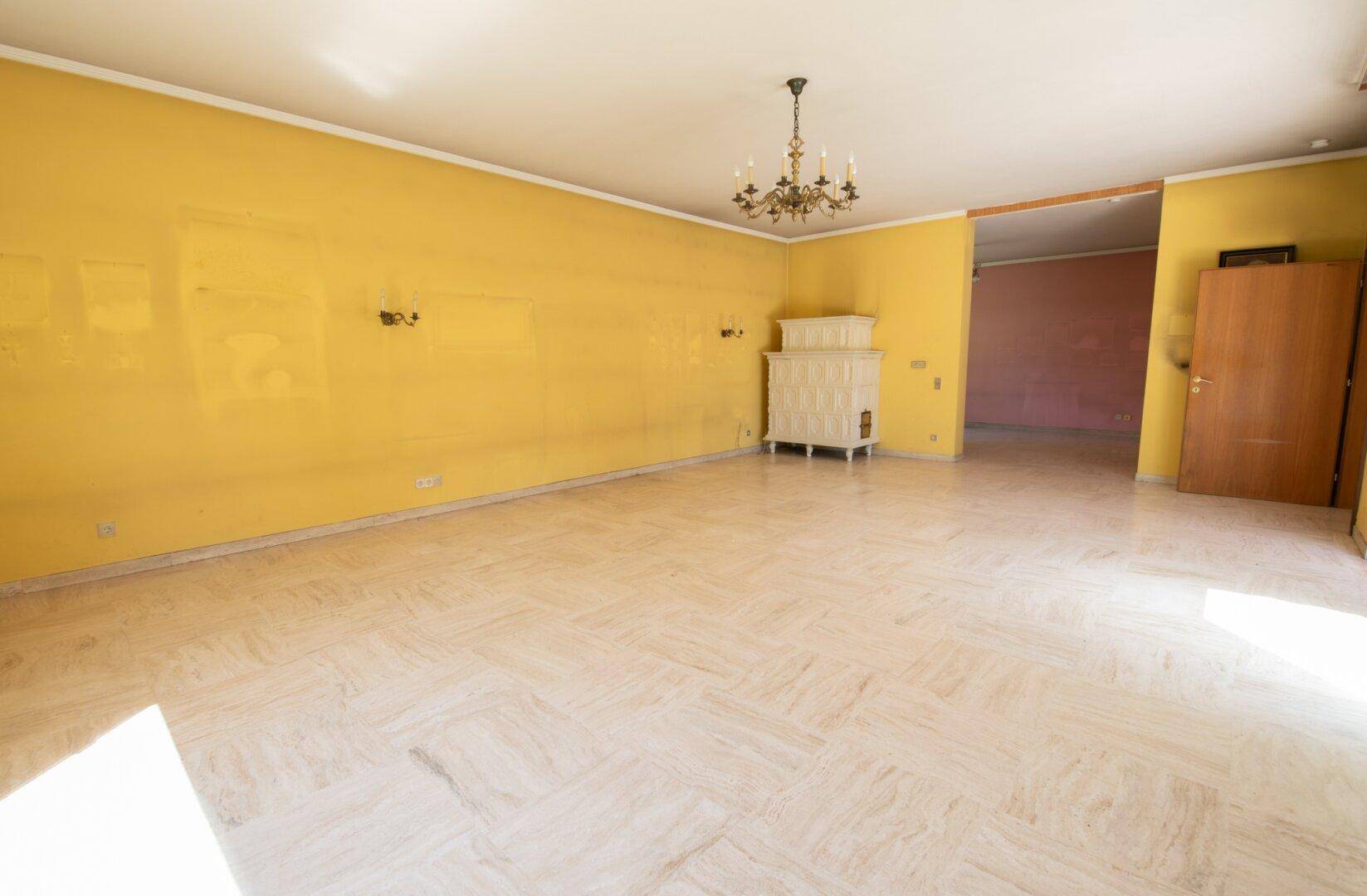 Großes Wohnzimmer mit traditionellem Kachelofen, gelben Wänden und Marmorboden.