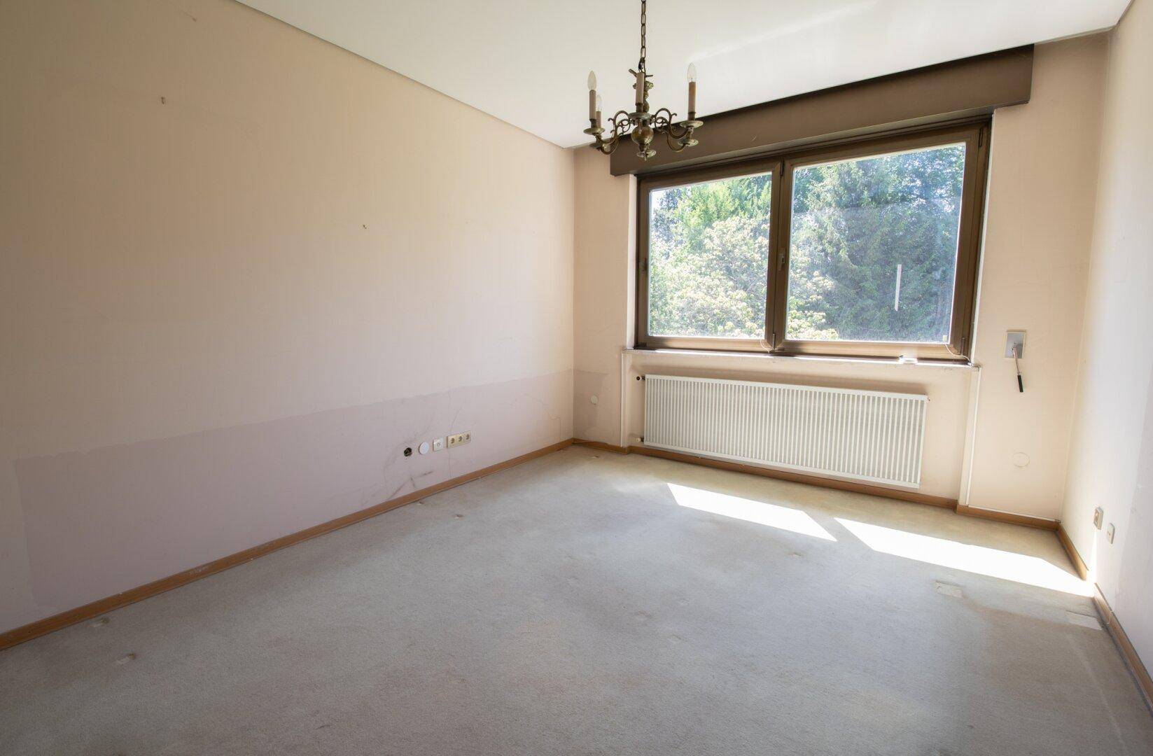 Geräumiges Schlafzimmer mit beigen Wänden, großem Fenster und Teppichboden.