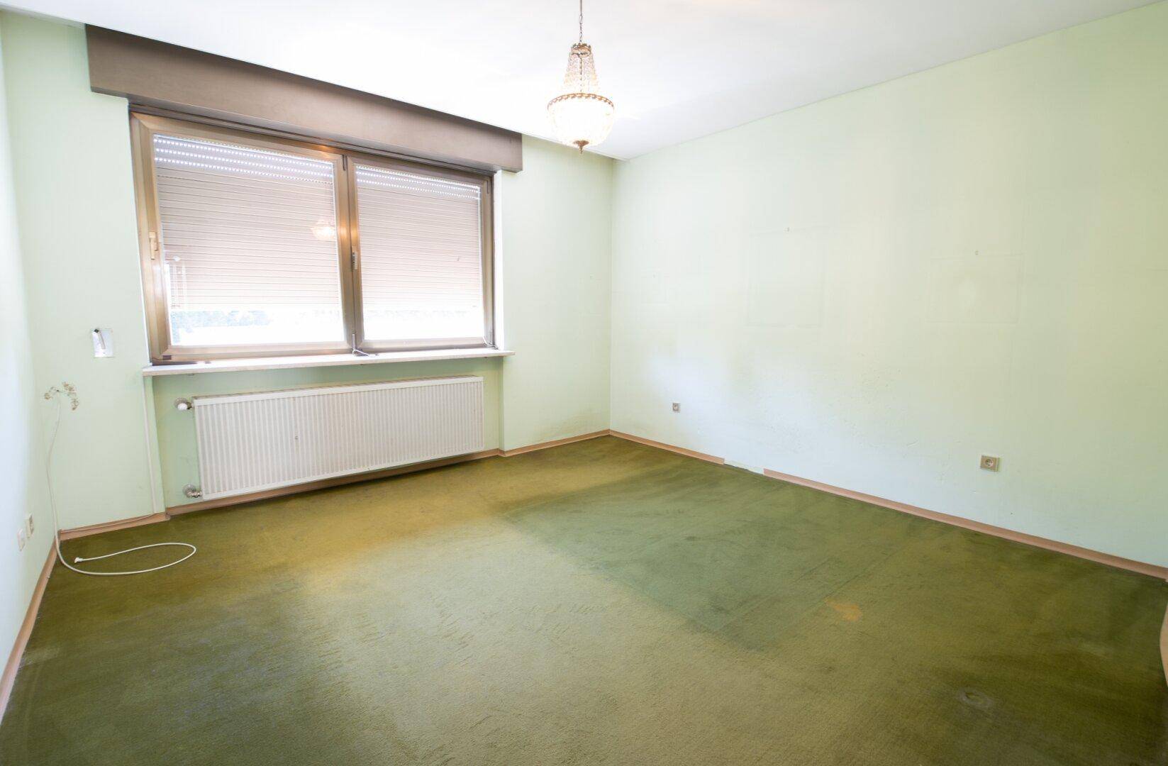 Helles Zimmer mit hellgrünen Wänden, Fenster und grünem Teppichboden.