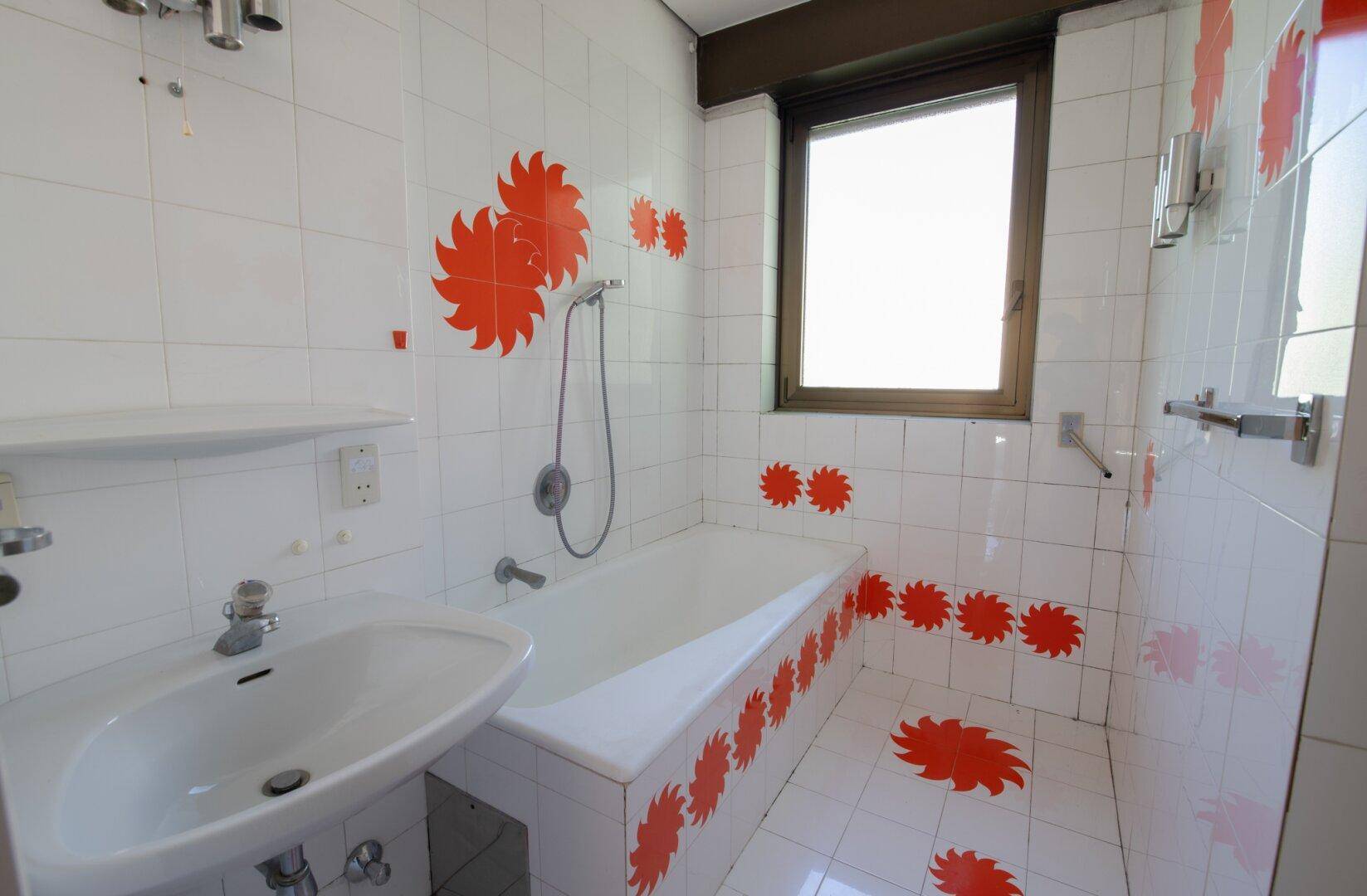 Badezimmer mit weißen Fliesen, orangefarbenen Dekorationen, Badewanne und Fenster.
