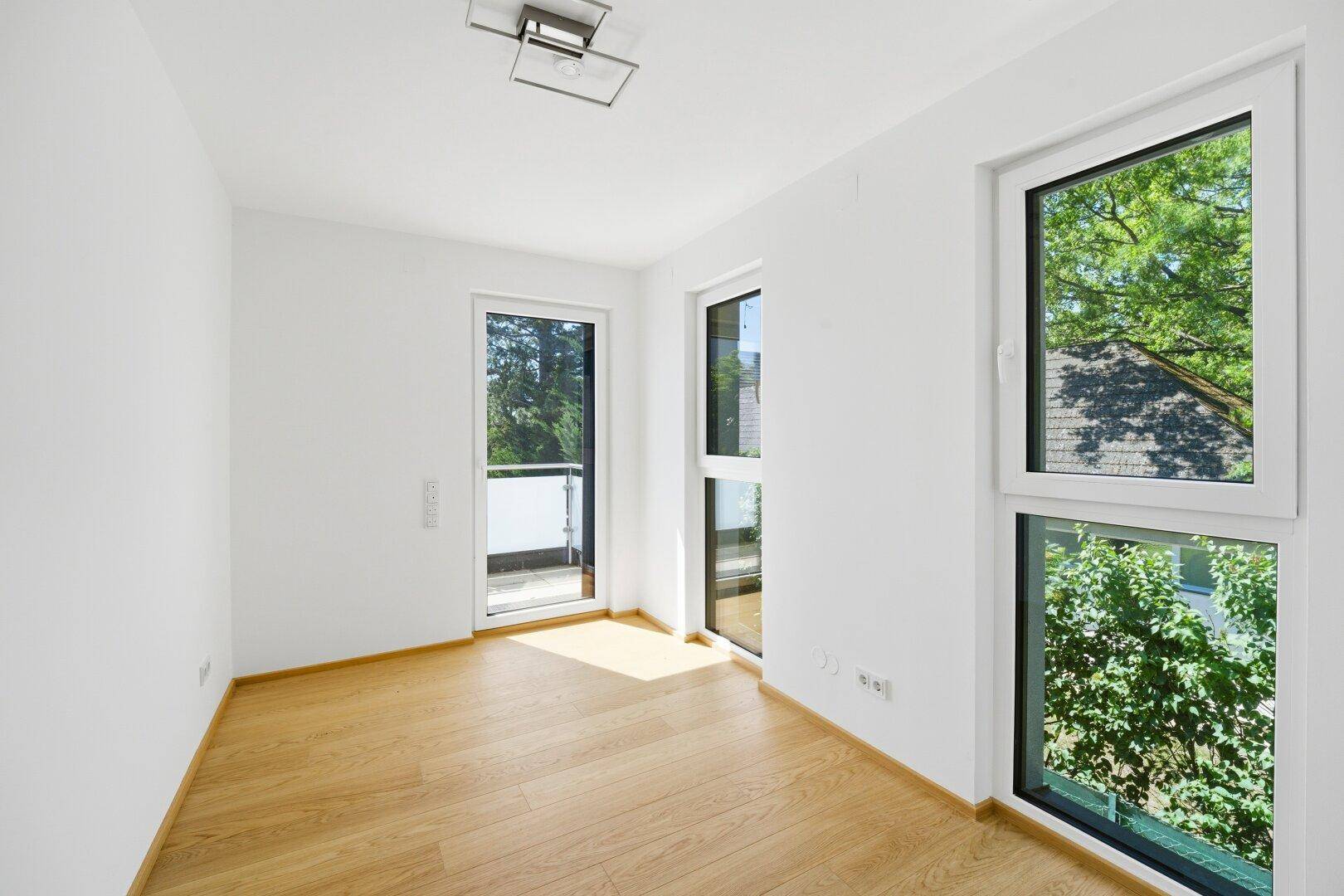 Helles Schlafzimmer mit Holzfußboden, Zugang zu einem französischen Balkon und Blick ins Grüne.