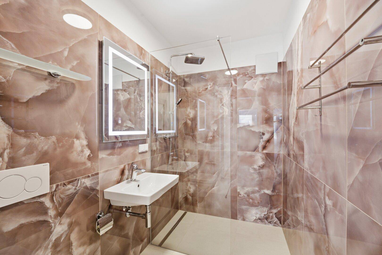 Elegantes Badezimmer mit braunen Marmorfliesen, begehbarer Dusche, Einzelwaschbecken und beleuchtetem Spiegel.