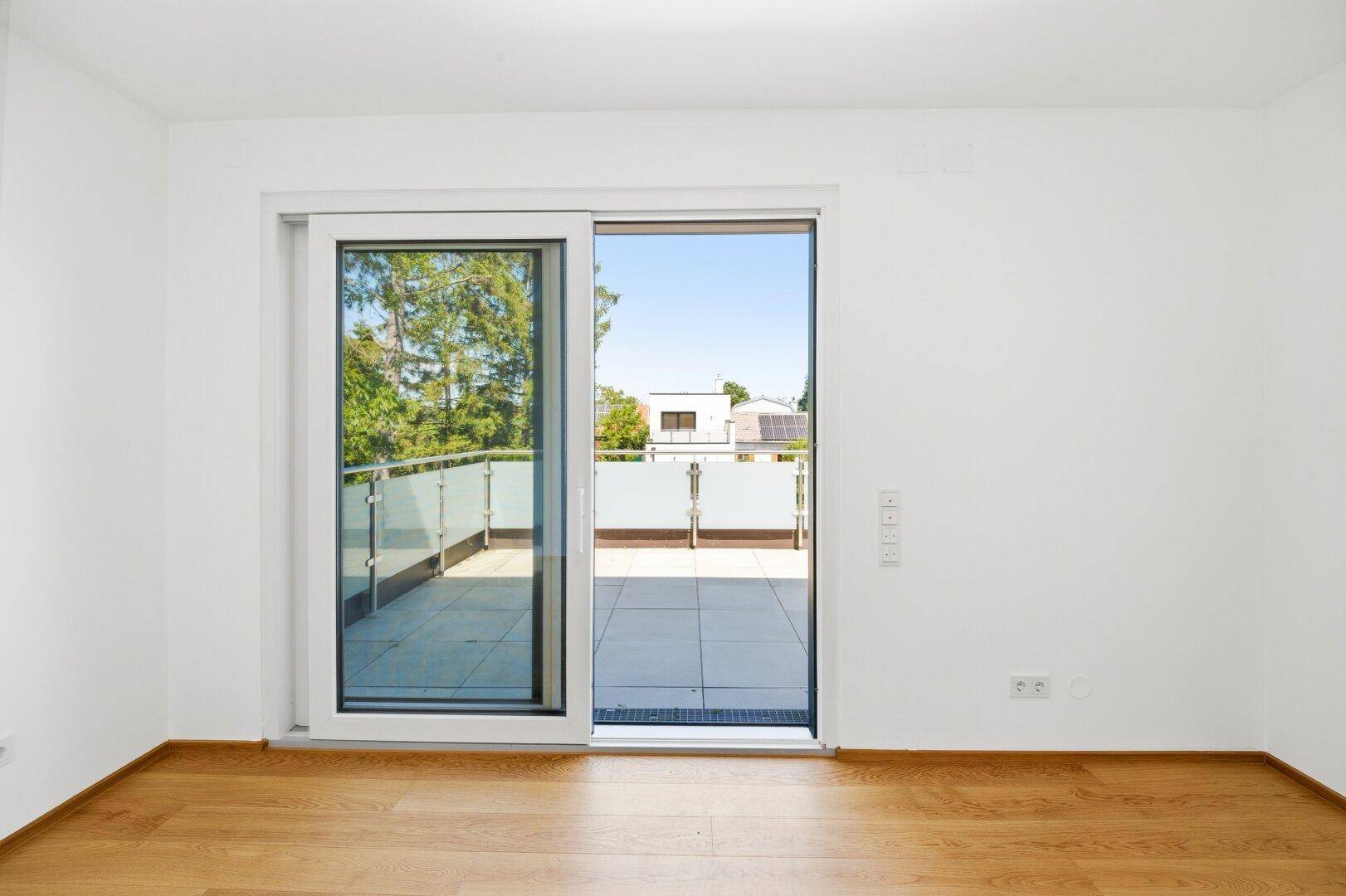 Geräumiges Schlafzimmer mit Holzfußboden und großen Schiebetüren, die auf eine Terrasse führen.