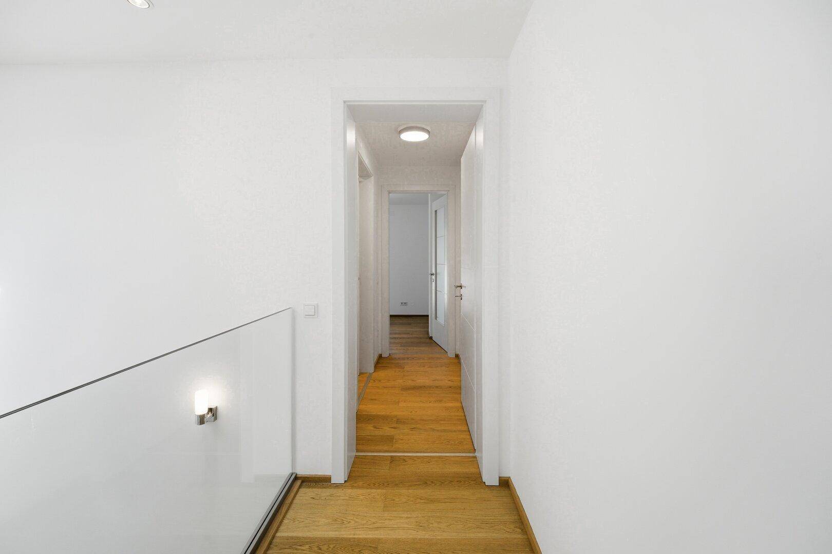 Heller Flur im Obergeschoss mit Holzfußboden, der zu weiteren Zimmern führt.
