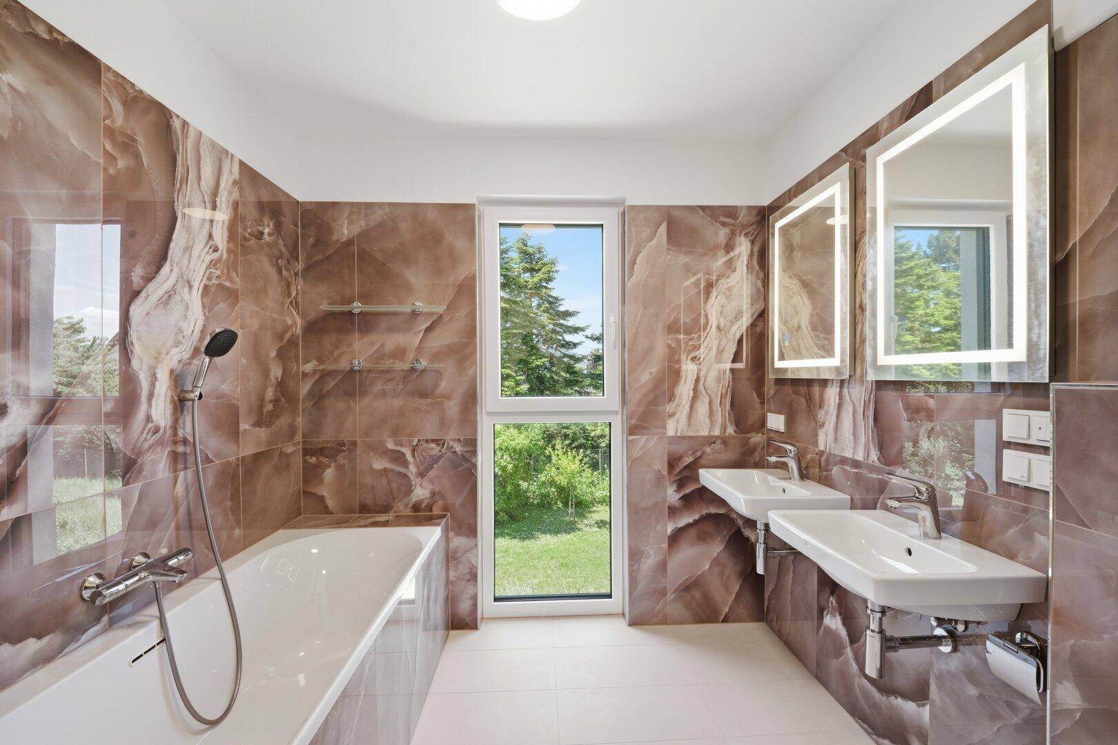 Modernes Badezimmer mit braunen Marmorfliesen, Doppelwaschbecken, Badewanne und Fenster mit Grünblick.